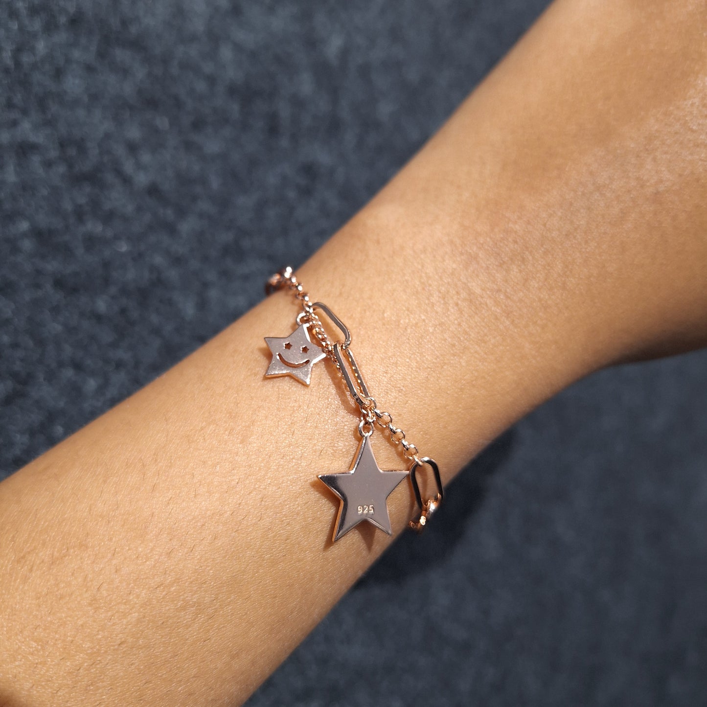 Rose gold bracelet with star charms on a wrist against a dark background