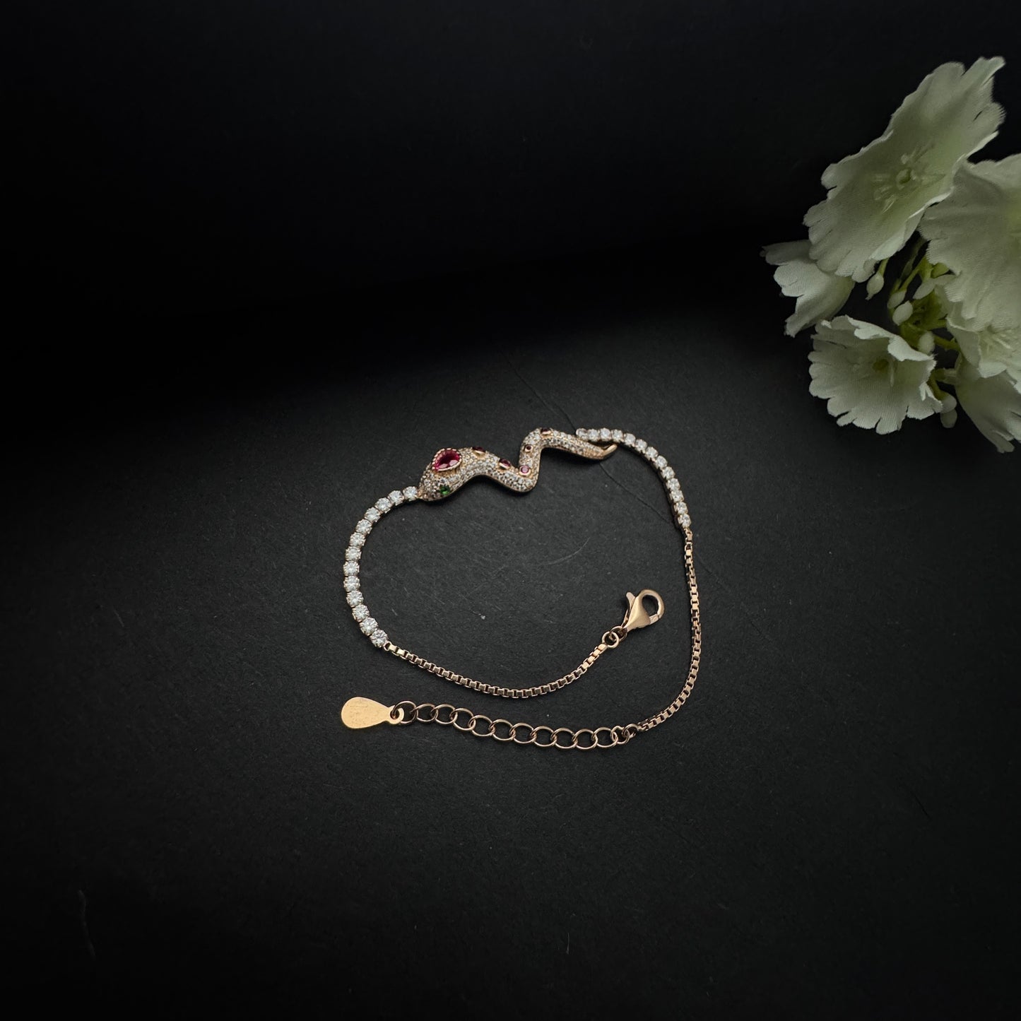 Gold bracelet with snake design on a dark surface with a white flower.