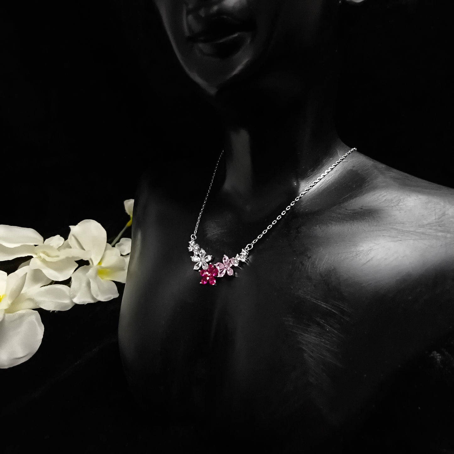 Necklace with floral design held by a hand with white flowers in the foreground
