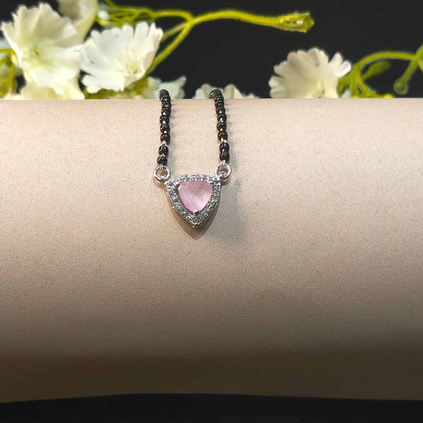 Ring with a pink gemstone on a beige stand with white flowers in the background