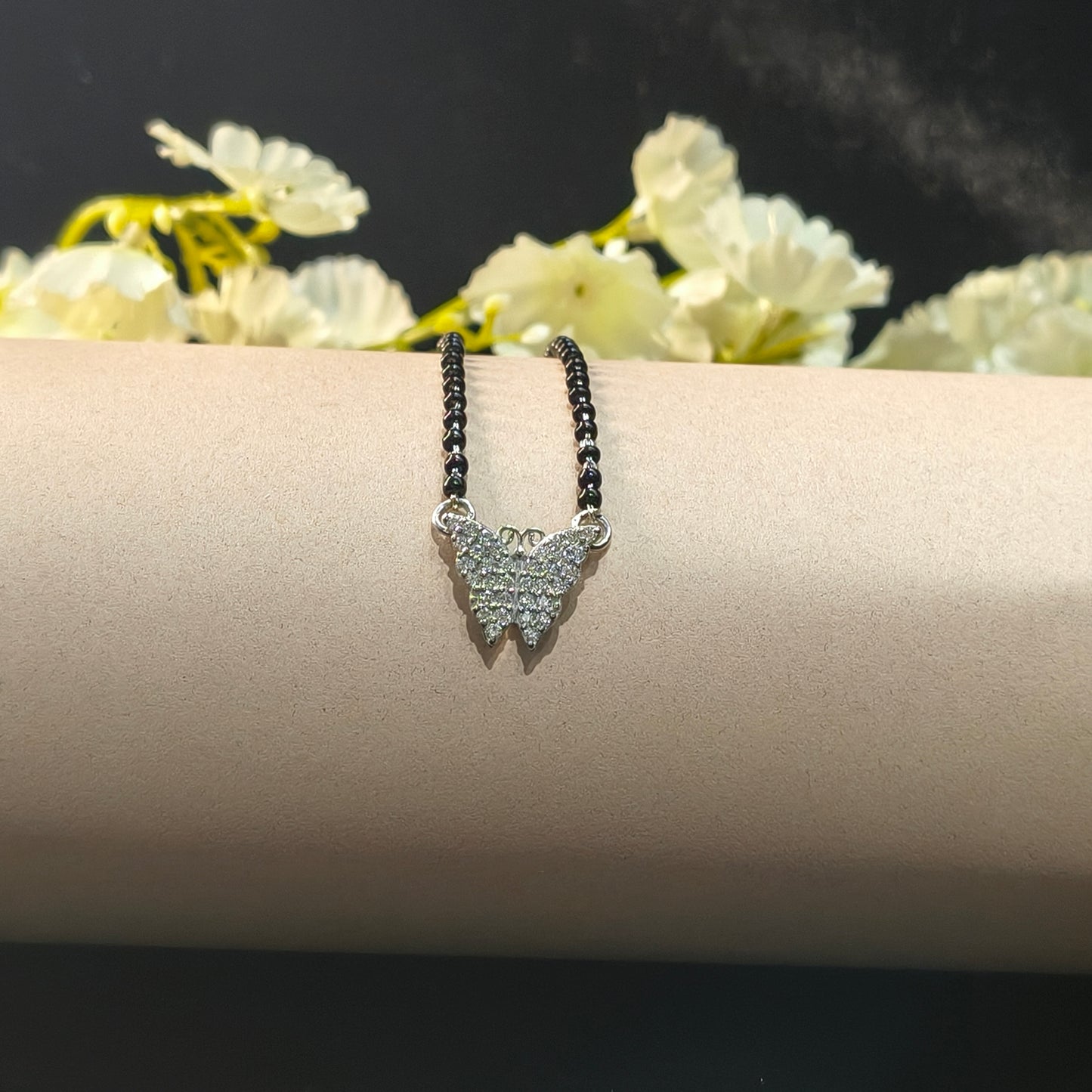 Silver bracelet with black stones on a beige arm against a dark background with light flowers.