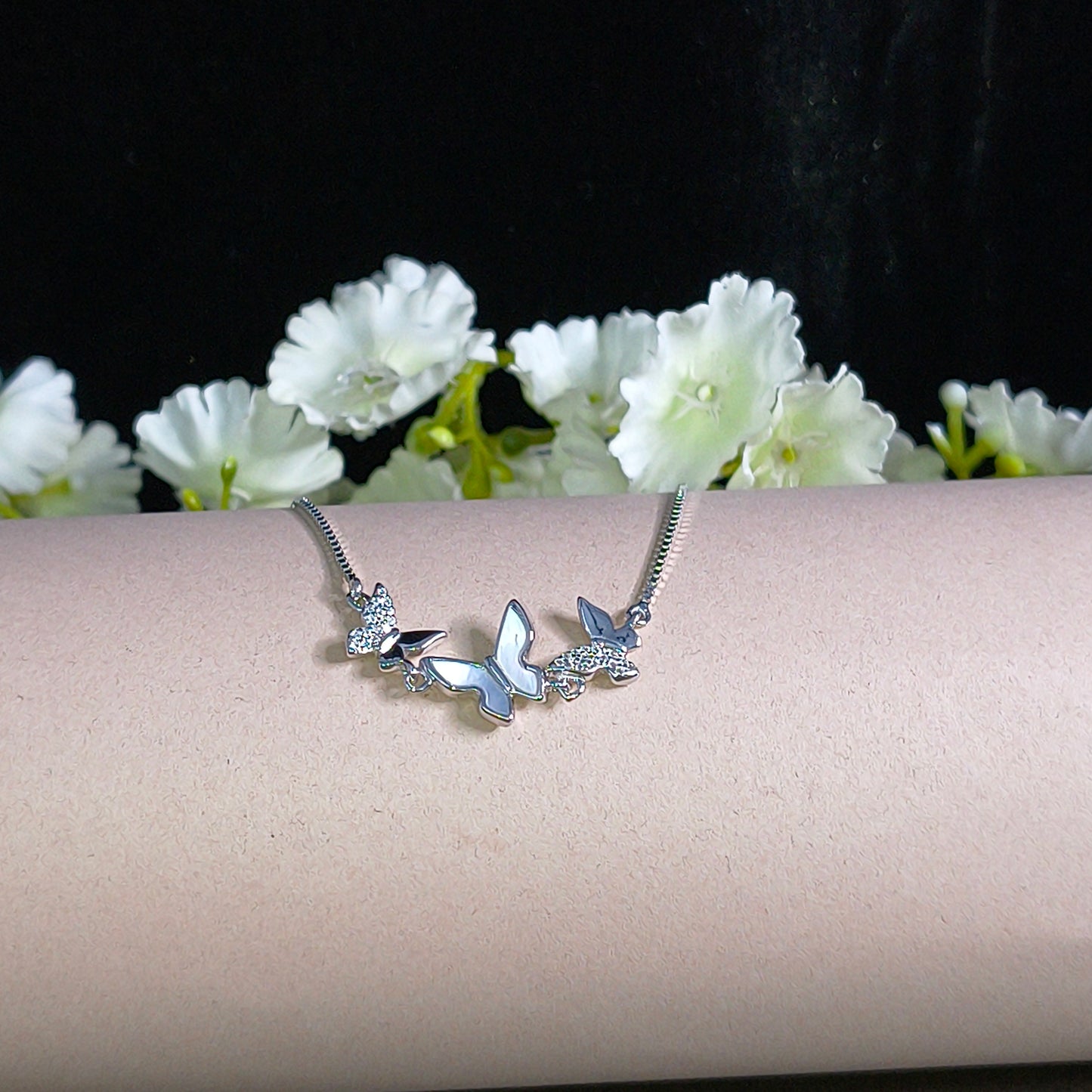 Butterfly-shaped silver bracelet on a pink stand with white flowers.