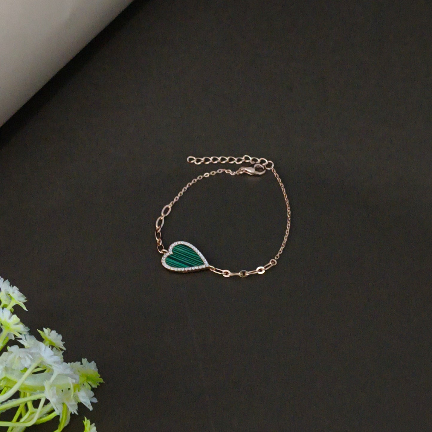 Gold bracelet with a green leaf charm on a dark background