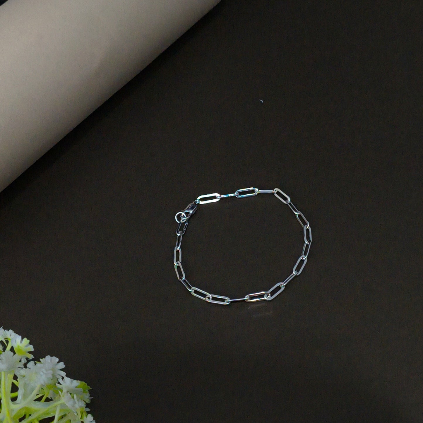 Silver chain bracelet on a dark surface with a floral edge.