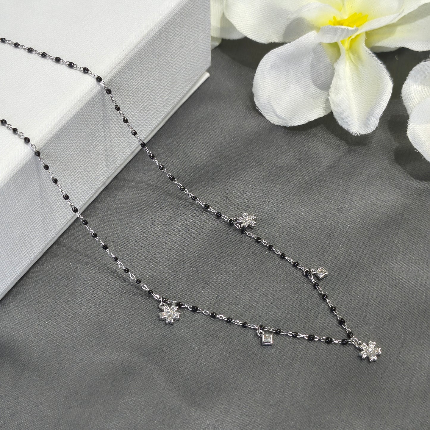 Silver necklace with black beads on a gray surface with white flowers.