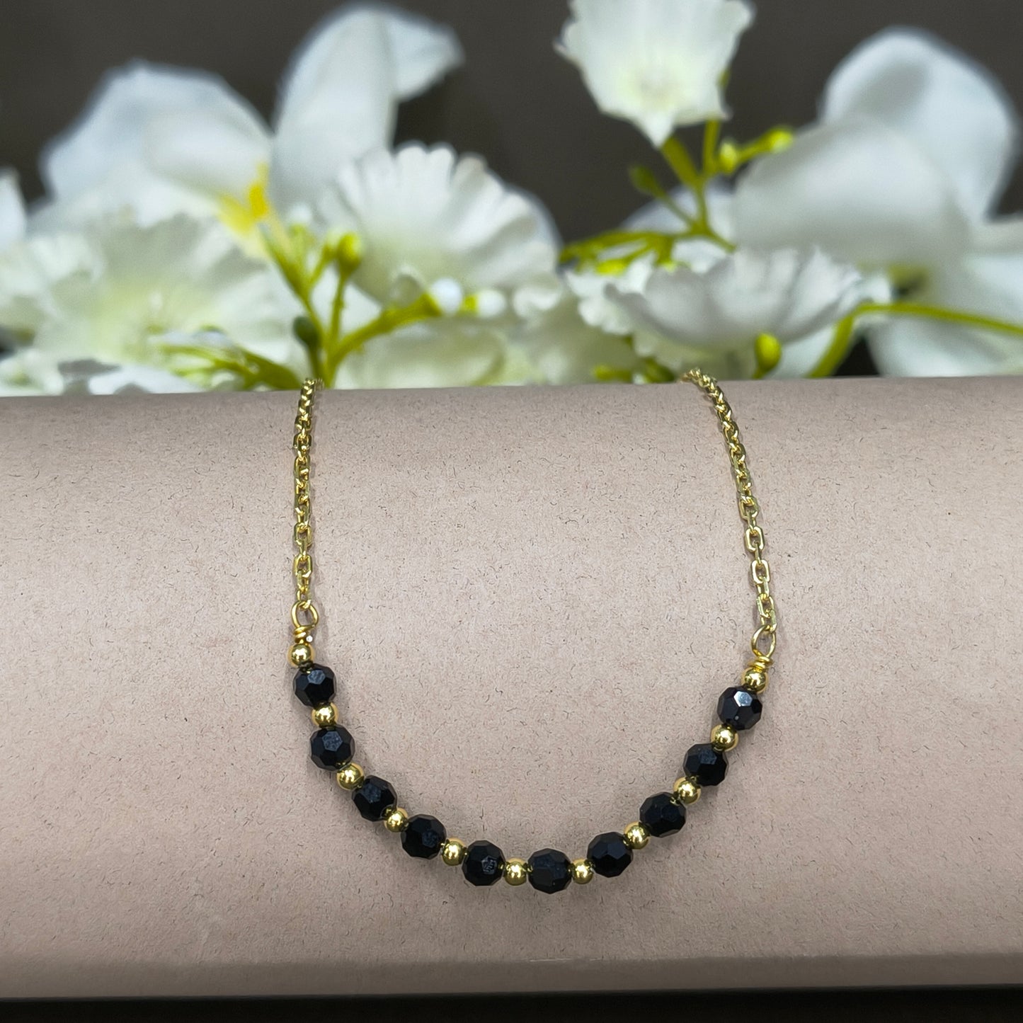Gold bracelet with black beads on a wrist against a white flower background