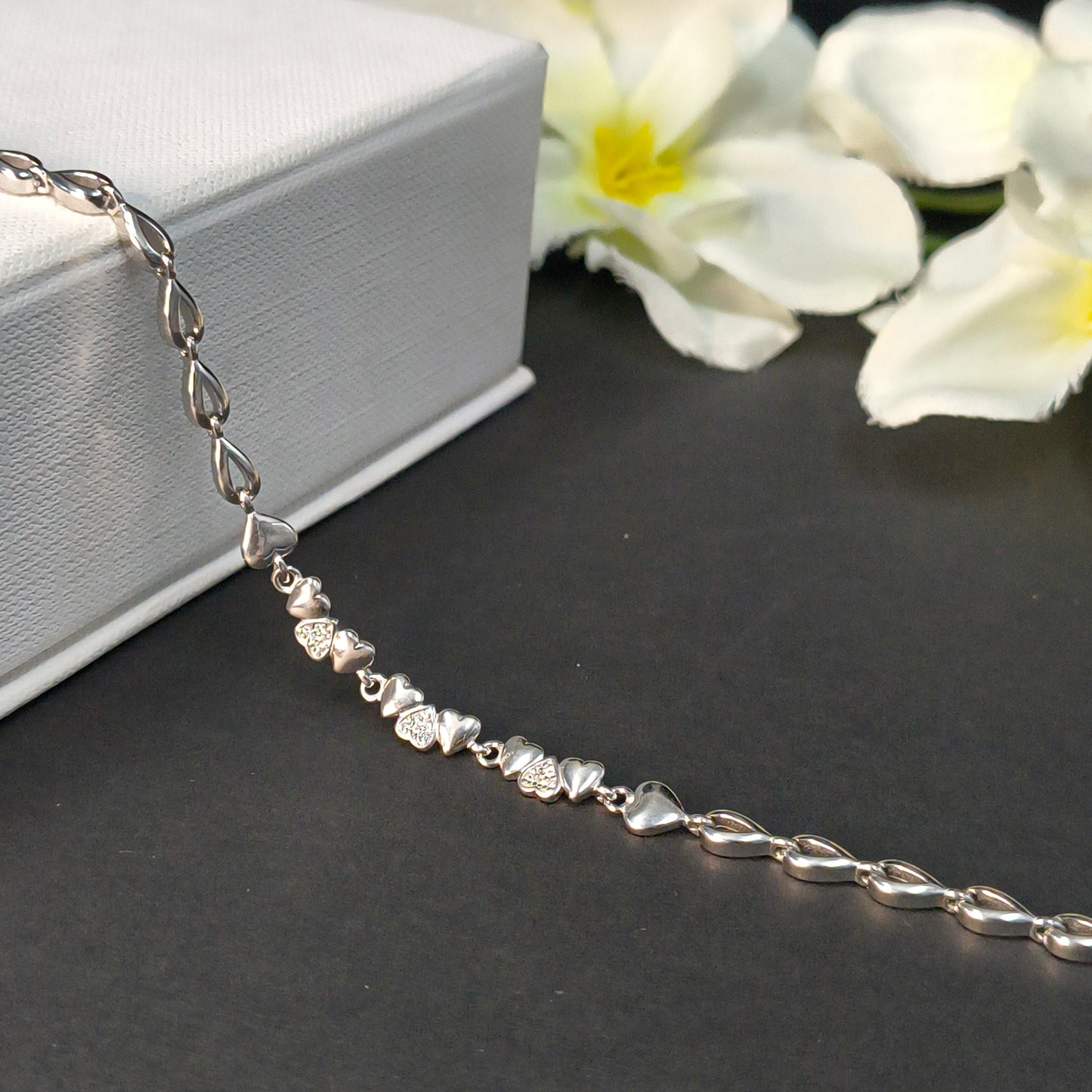 Silver bracelet with heart-shaped charms on a dark surface with flowers in the background