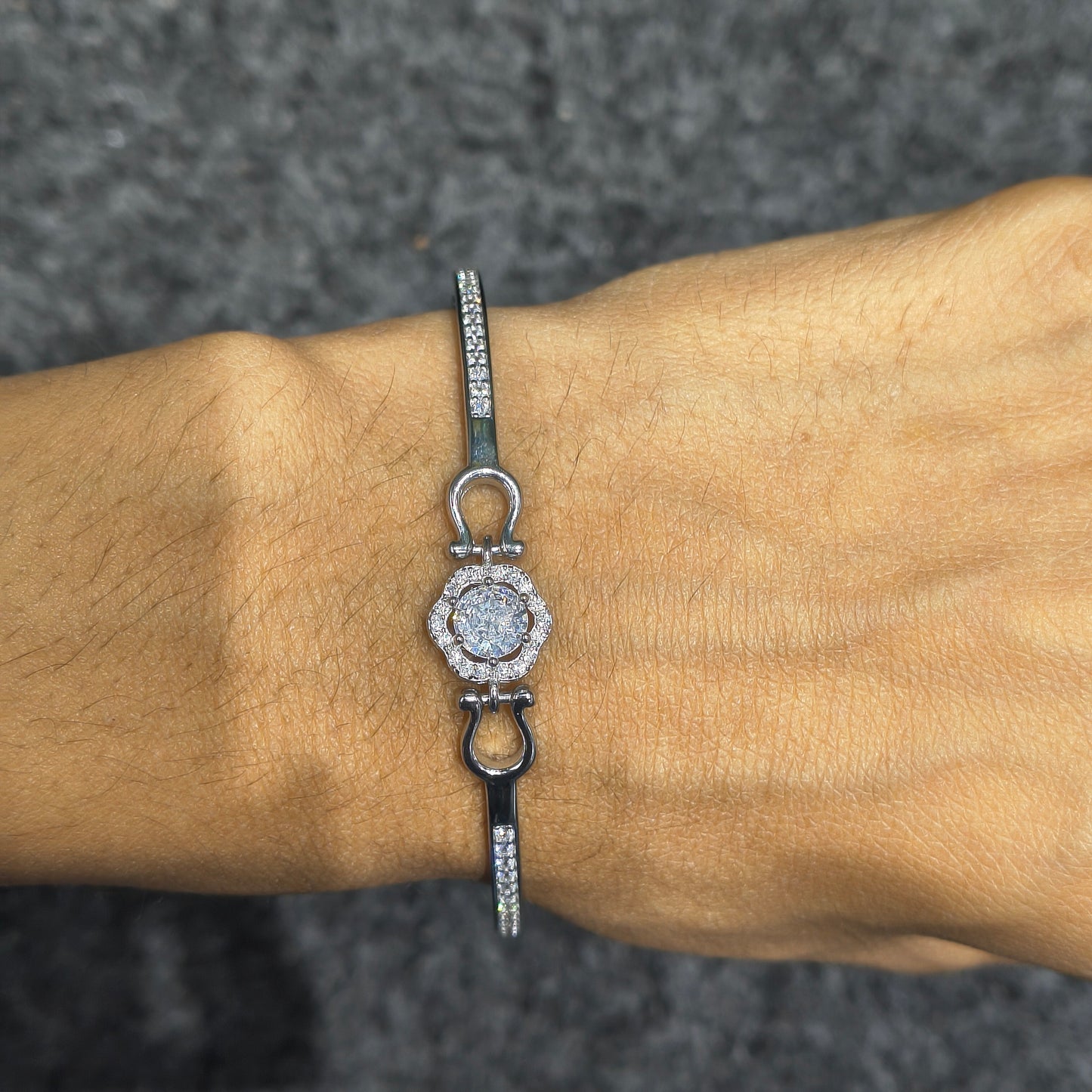 Silver bracelet with a decorative clasp on a wrist against a dark background