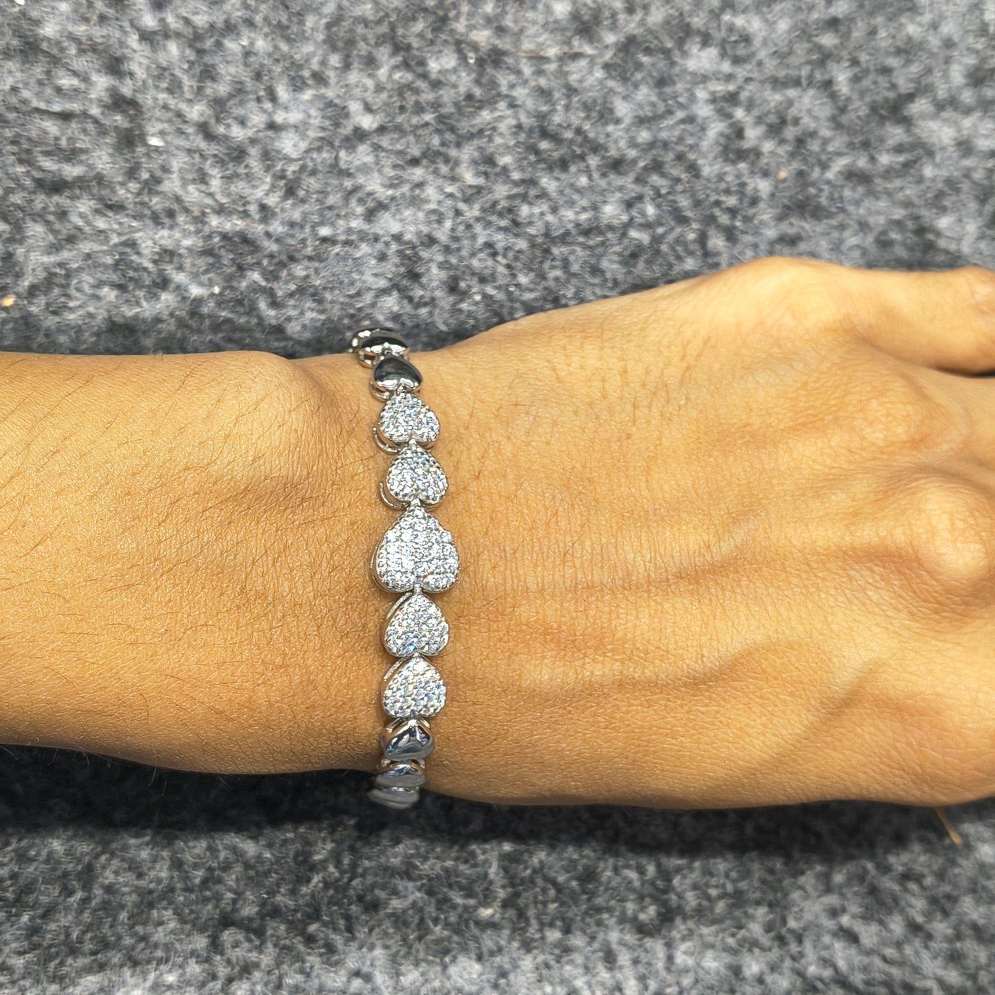 Silver bracelet with heart-shaped diamonds on a wrist against a gray background