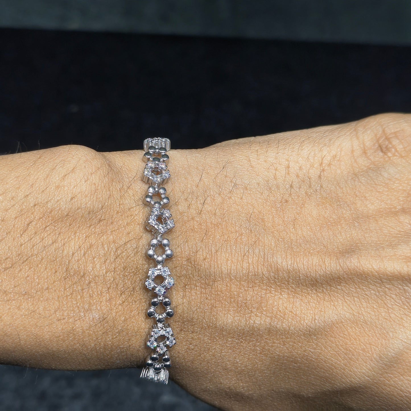 Silver bracelet with diamonds on a wrist against a dark background