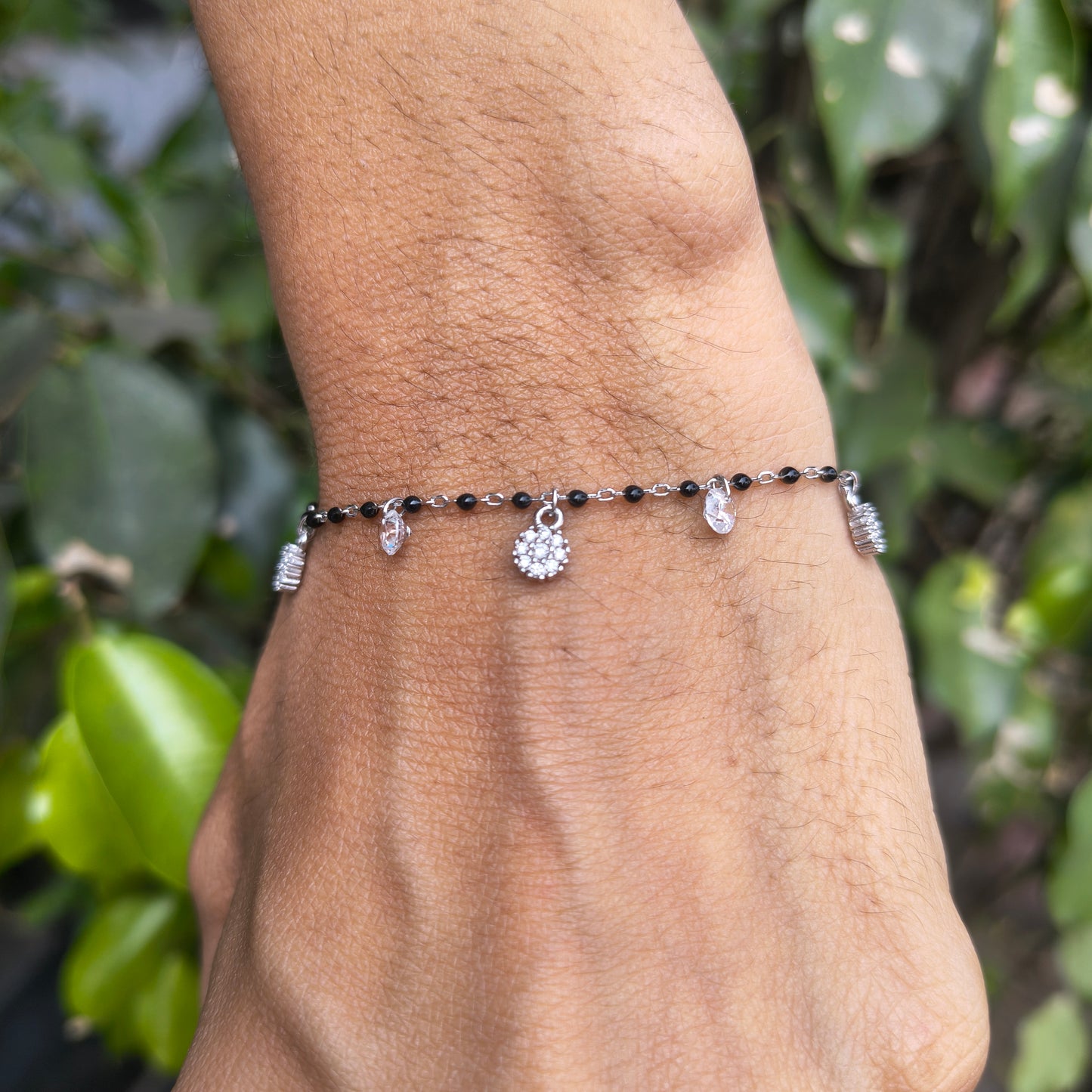 Bracelet with black beads and silver charms on a wrist against a green leafy background