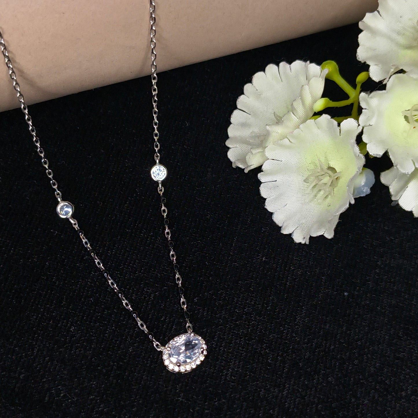 Silver chain necklace with gemstones on a black background with white flowers.