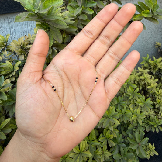 Hand holding a delicate necklace with green foliage in the background
