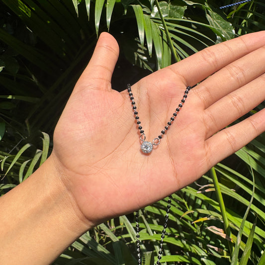 Hand holding a necklace with a green leafy background