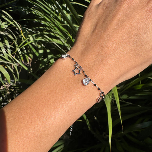 Bracelet with star and heart charms on a wrist against a natural background
