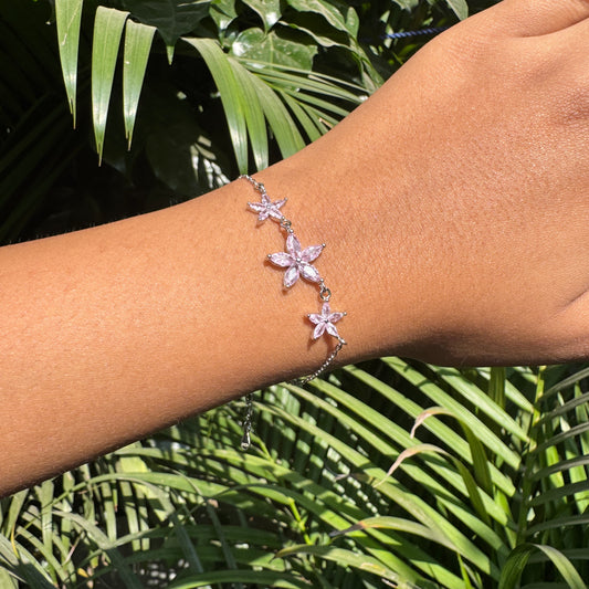 Bracelet with pink flower charms on a wrist against a green leafy background