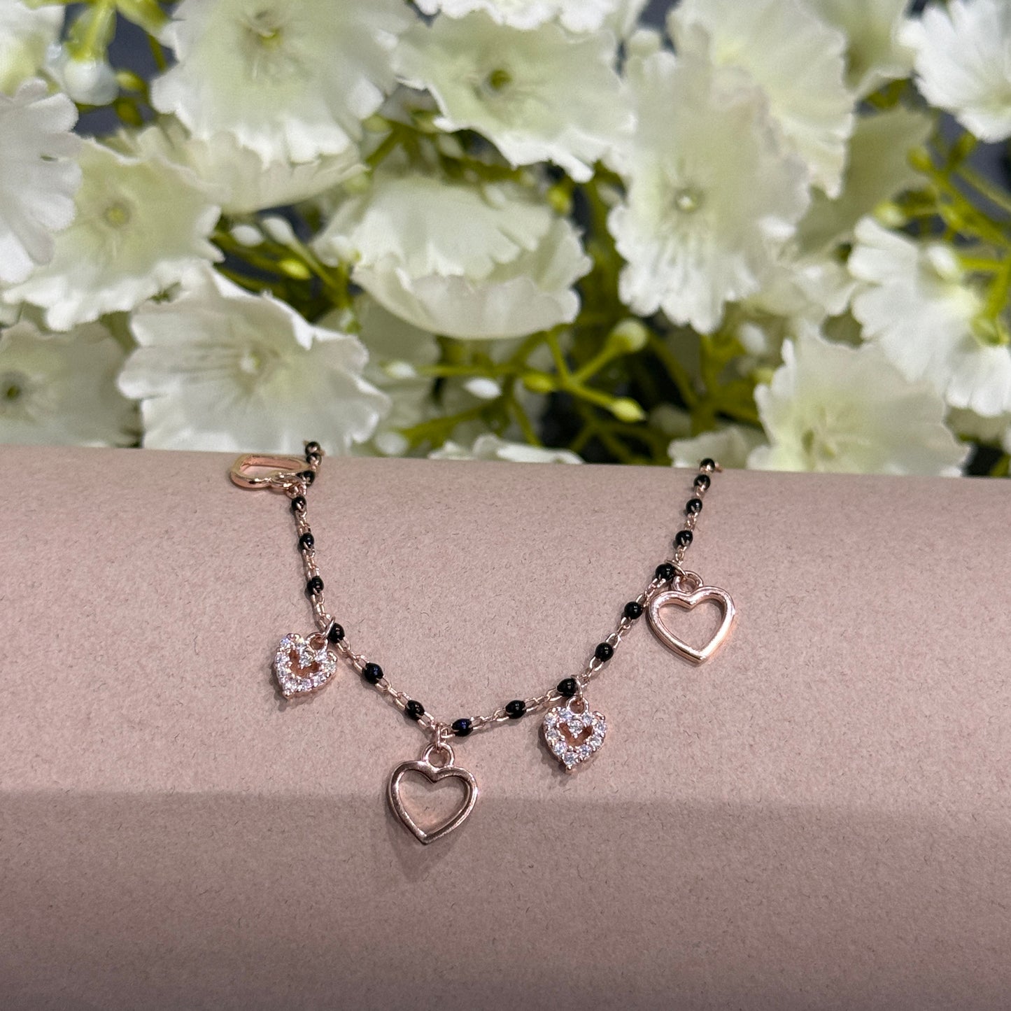 Necklace with heart-shaped pendants on a beige surface with white flowers in the background