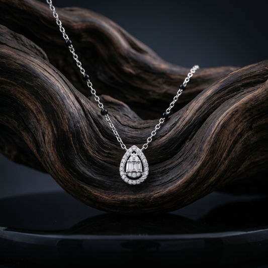 Silver necklace with a teardrop-shaped pendant on a dark, wavy wooden surface