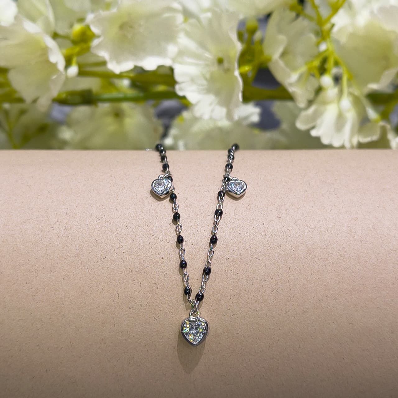 Necklace with heart-shaped pendants on a wrist against a floral background