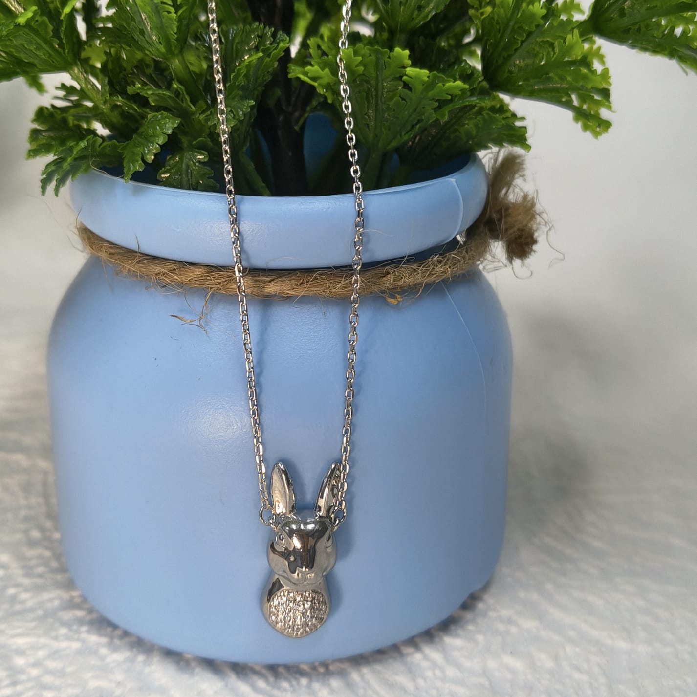 Silver rabbit pendant necklace hanging from a plant pot with a white background