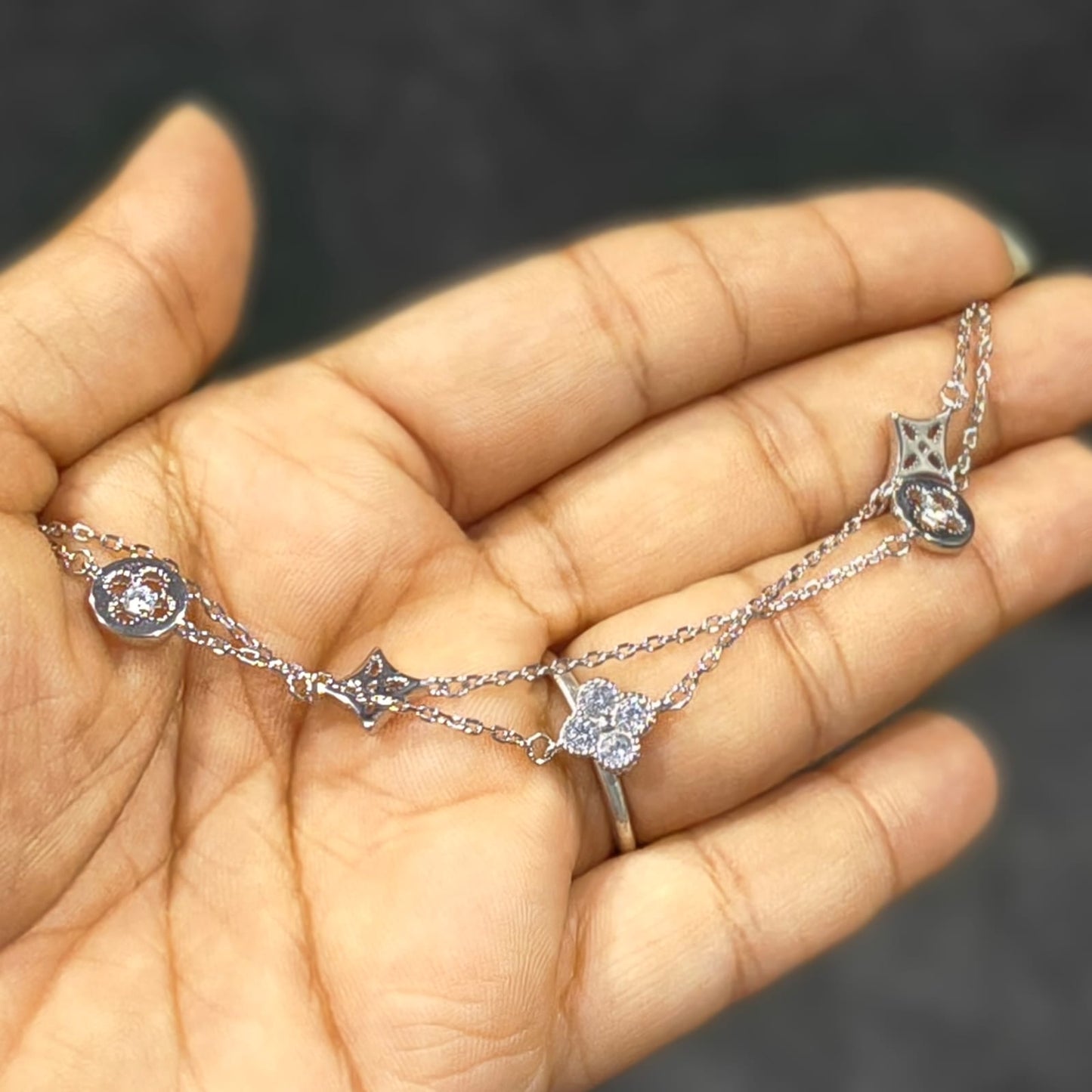 Silver bracelet with star and heart charms held in a hand against a dark background