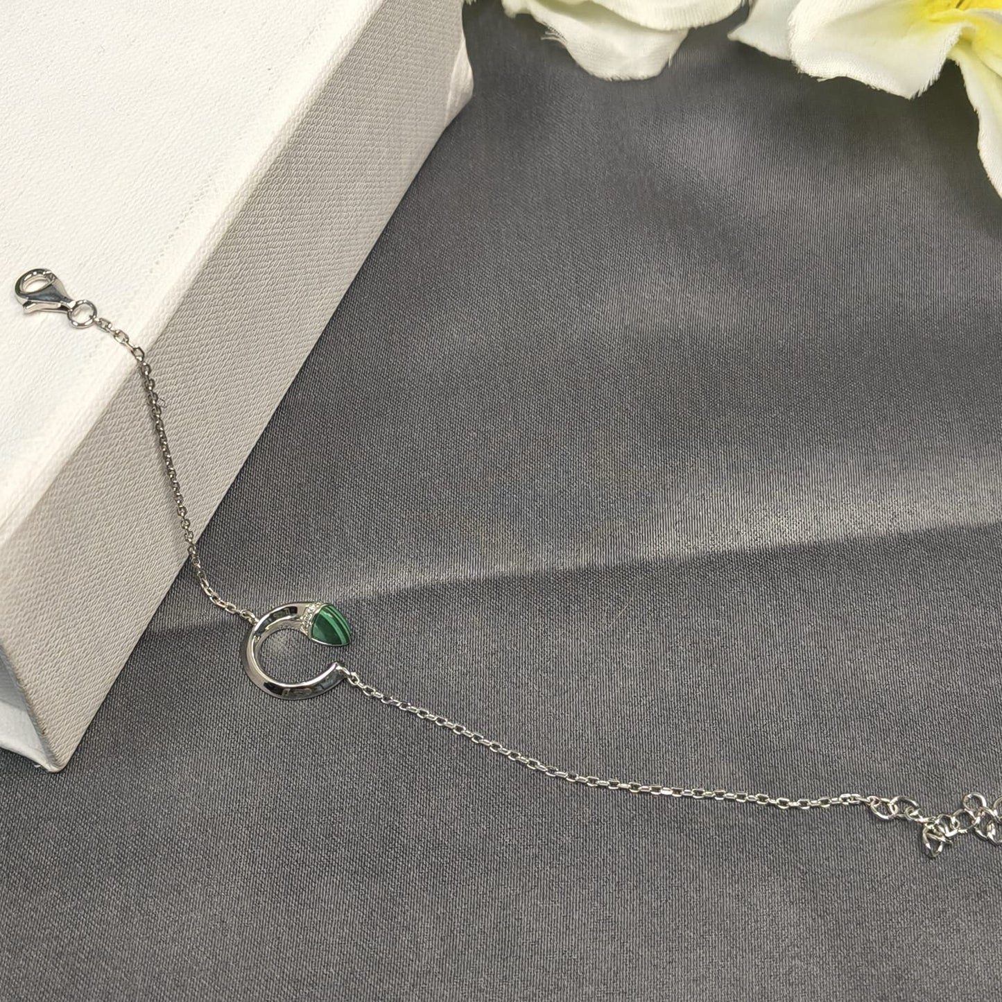 Silver bracelet with a green gemstone on a gray surface with white flowers in the background