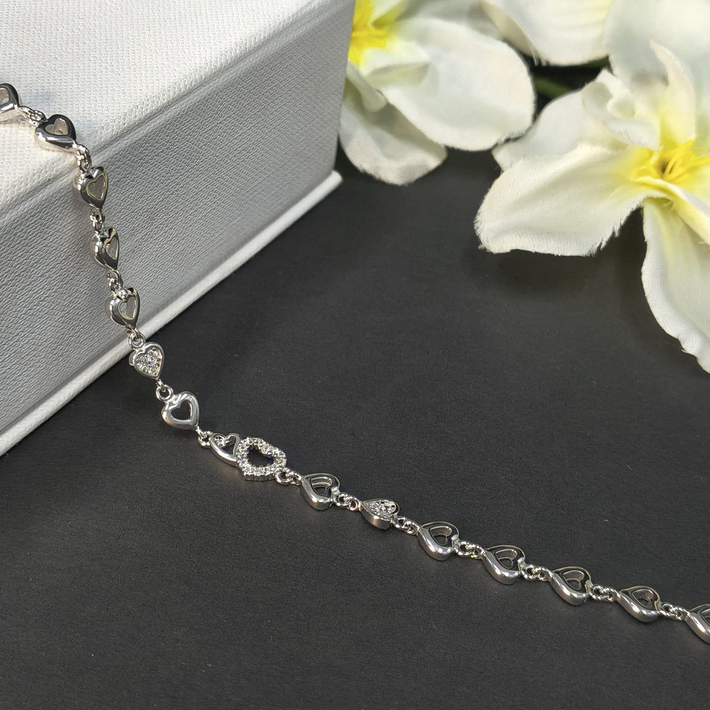 Silver bracelet with heart designs on a dark surface with white flowers.