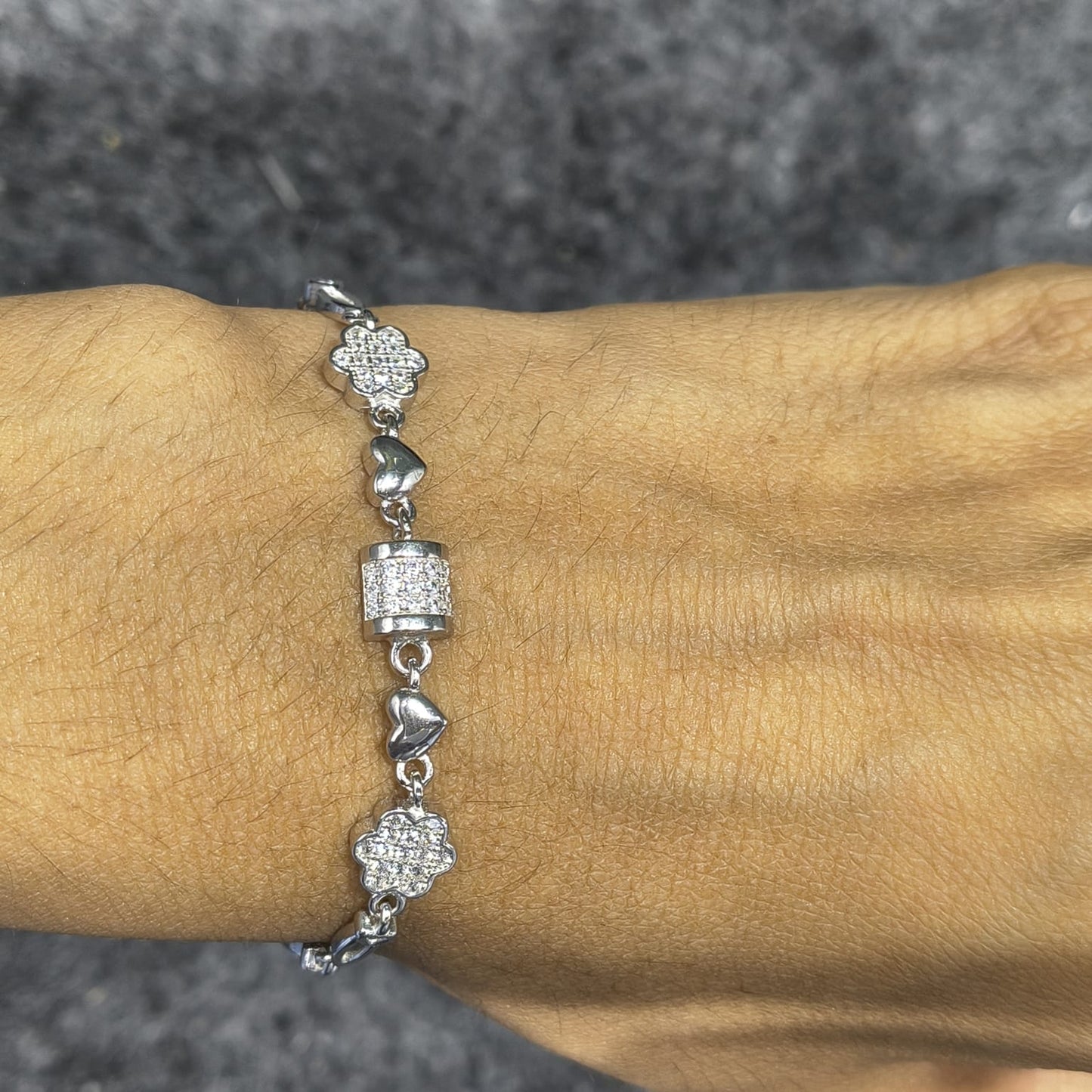 Silver bracelet with heart and floral designs on a wrist against a gray background