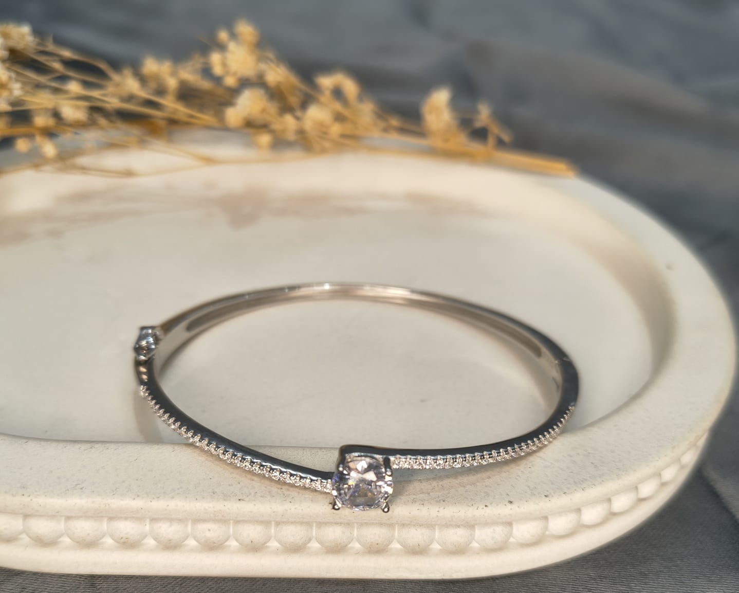 Silver bracelet with a diamond on a white dish with dried flowers