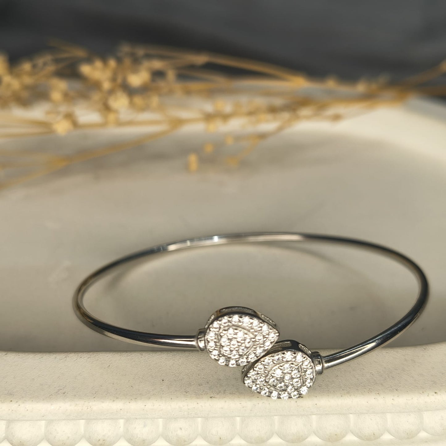 Silver bracelet with two round embellishments on a textured surface with dried flowers.