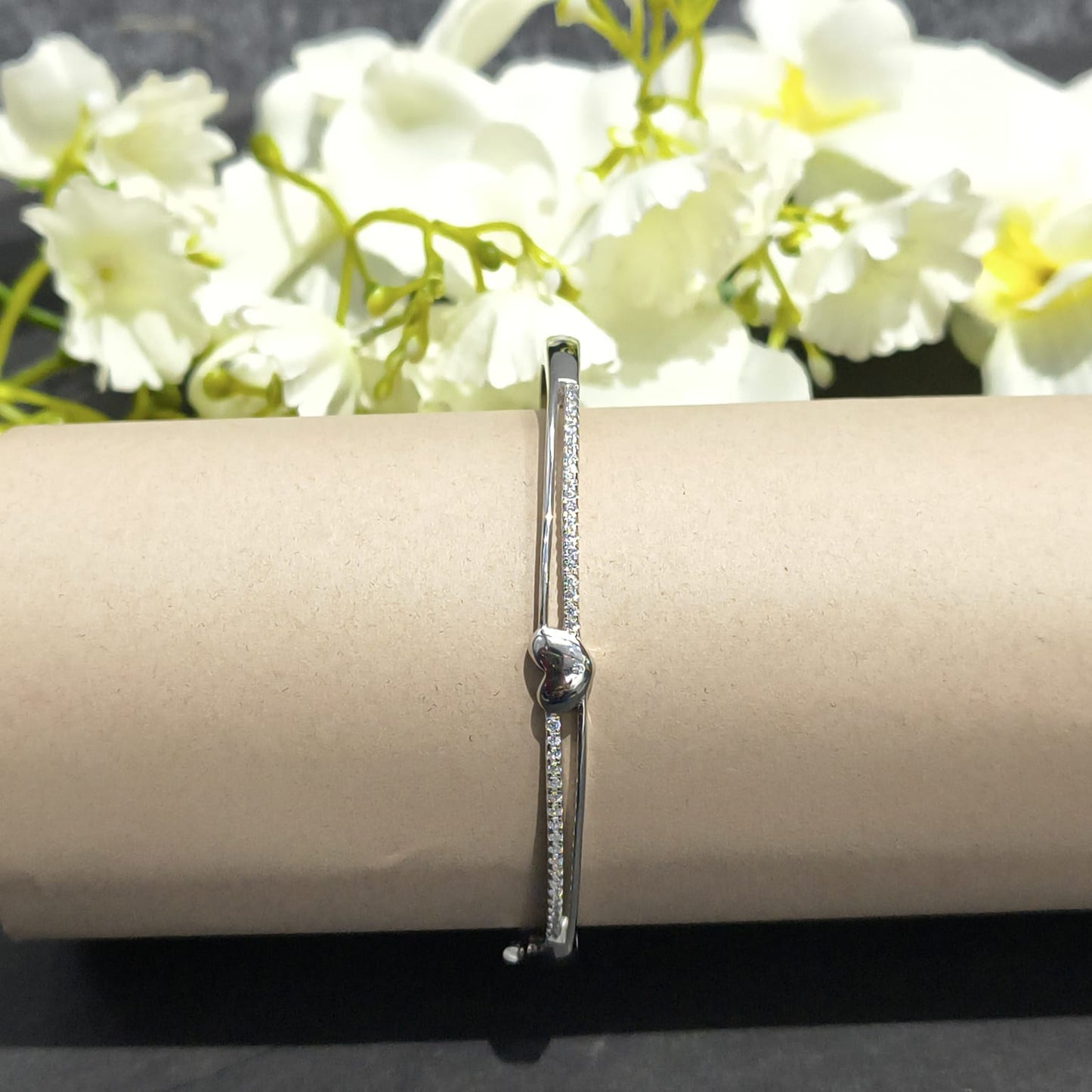 Silver bracelet on a cylindrical object with white flowers in the background
