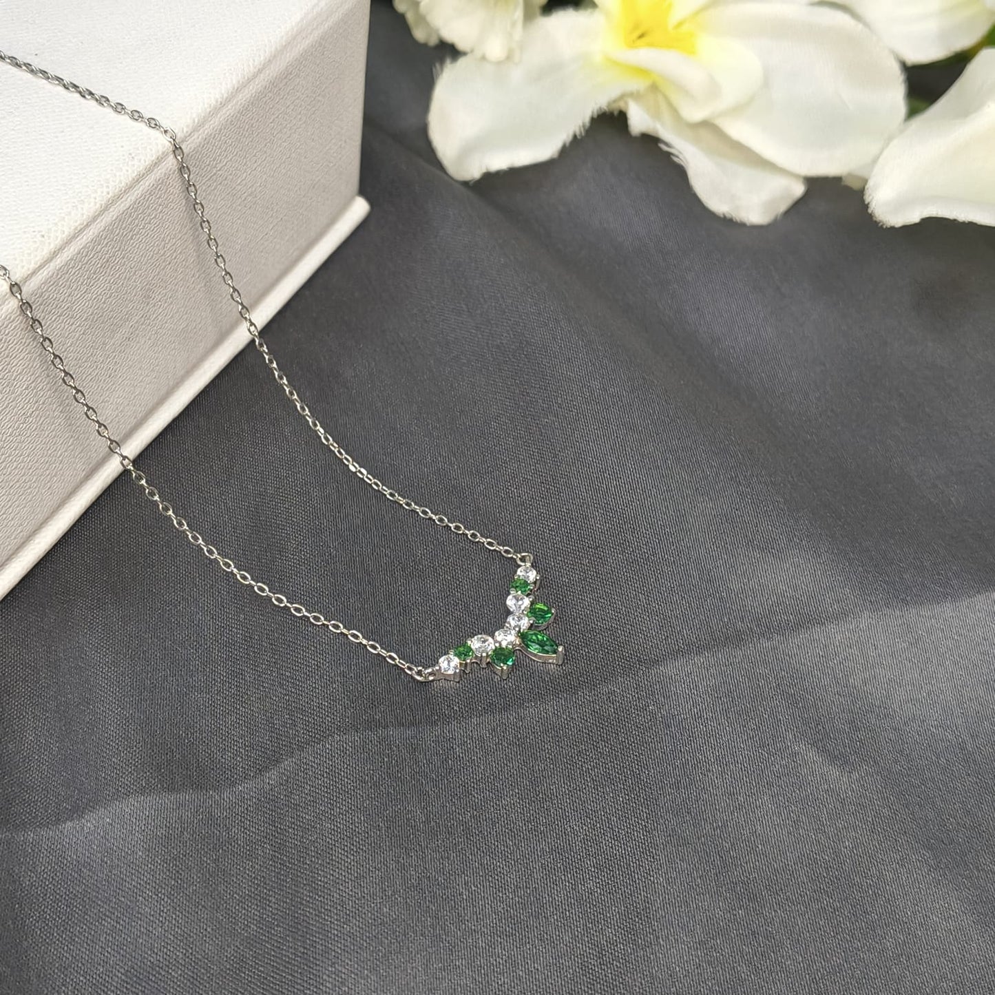 Necklace with green gemstones on a gray surface with flowers in the background