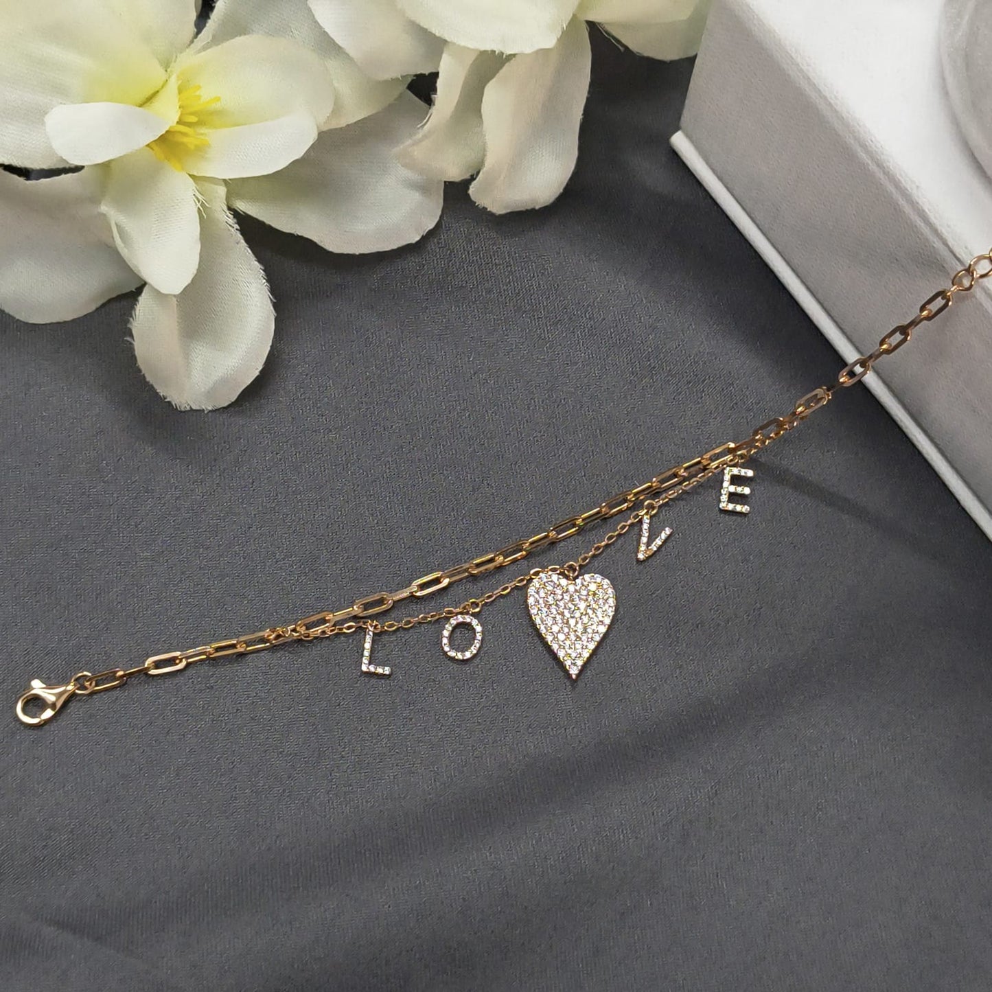 Gold bracelet with 'LOVE' charms on a gray surface with white flowers.