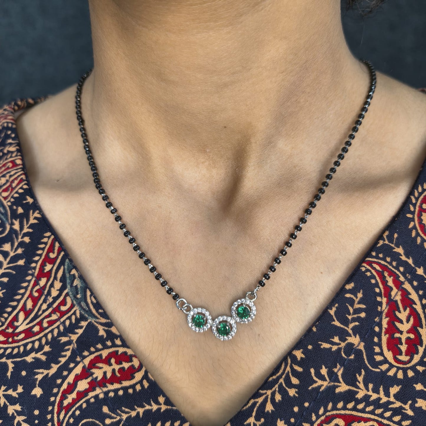 Necklace with green gemstones worn by a person in a patterned garment