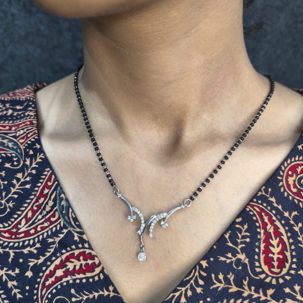 Necklace with a silver pendant worn by a person against a patterned garment.