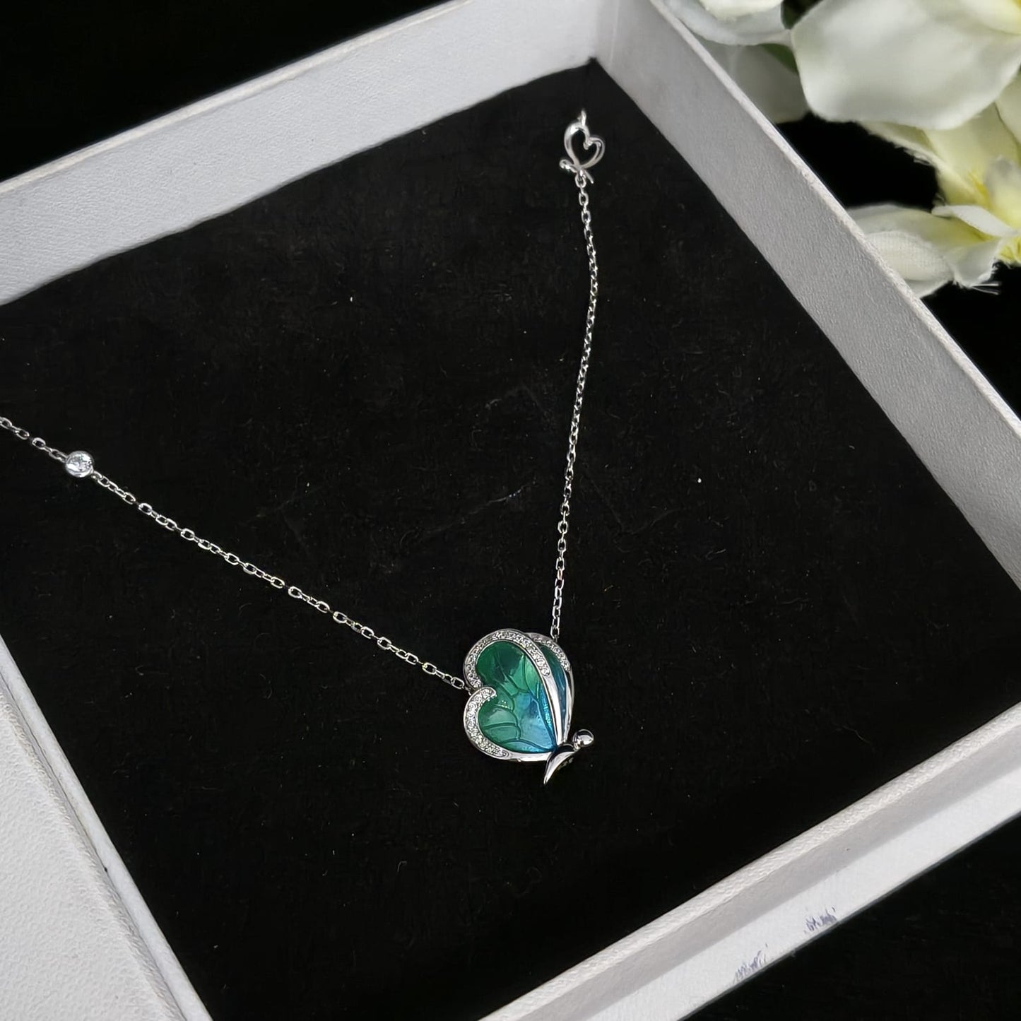 Butterfly-shaped necklace on a black cushion in a jewelry box with flowers in the background
