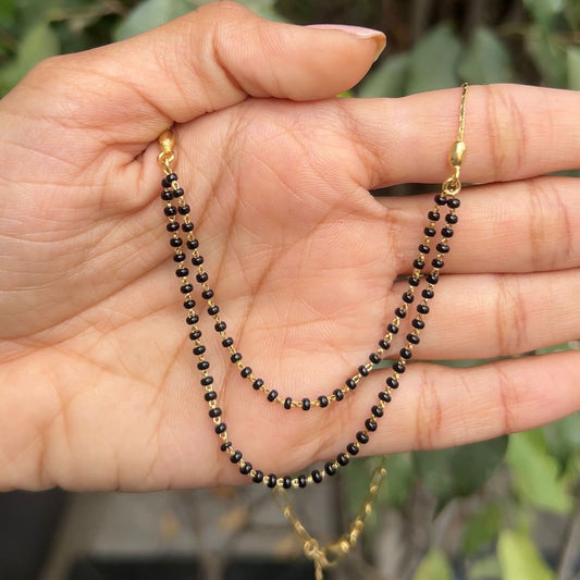 Hand holding two black beaded necklaces with gold clasps against a blurred green background