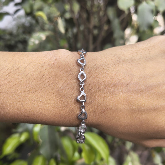 Silver bracelet with heart-shaped charms on a wrist against a blurred green background
