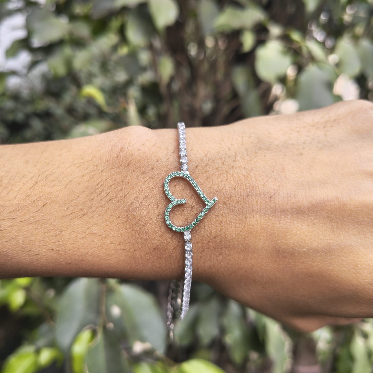 Bracelet with a heart design on a wrist against a blurred green background