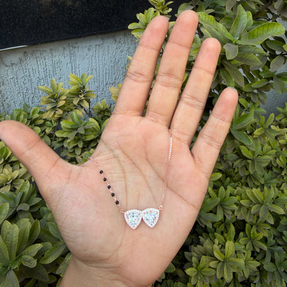 Hand holding a small silver earring with green foliage in the background