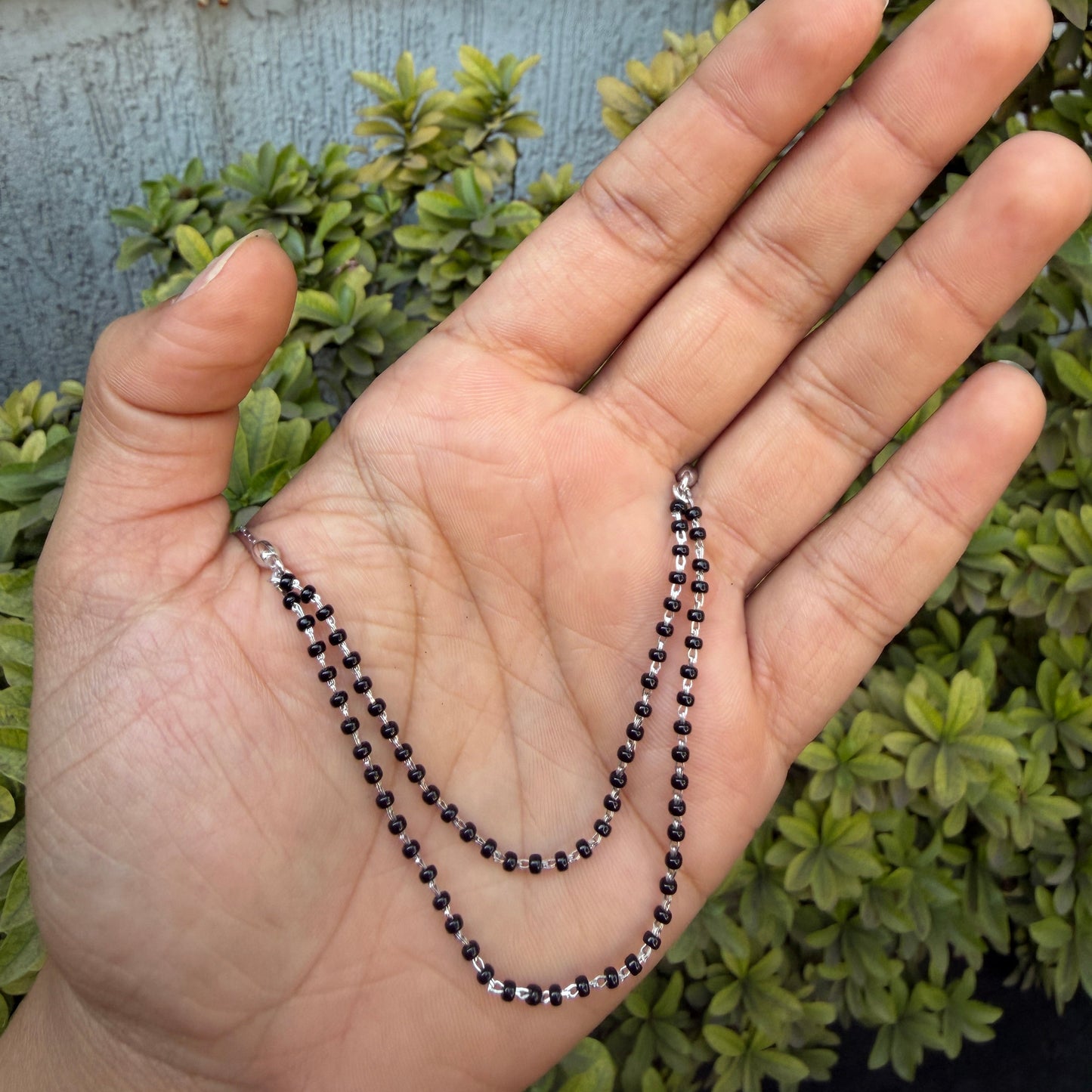 Hand holding a black beaded necklace with green foliage in the background