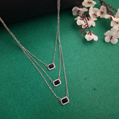 Silver necklace with black stones on a green surface with white flowers.