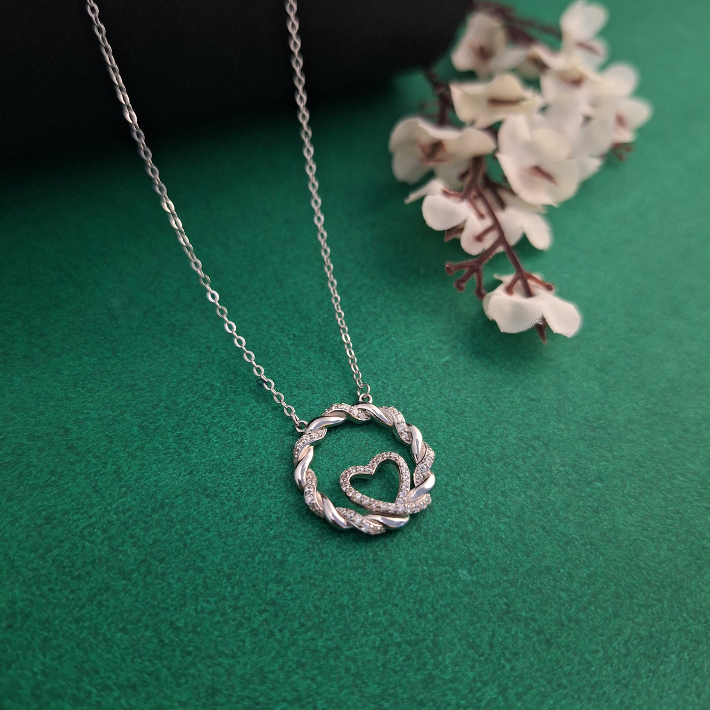 Silver necklace with a heart-shaped pendant on a green background