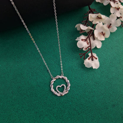 Silver necklace with a heart-shaped pendant on a green background with white flowers.