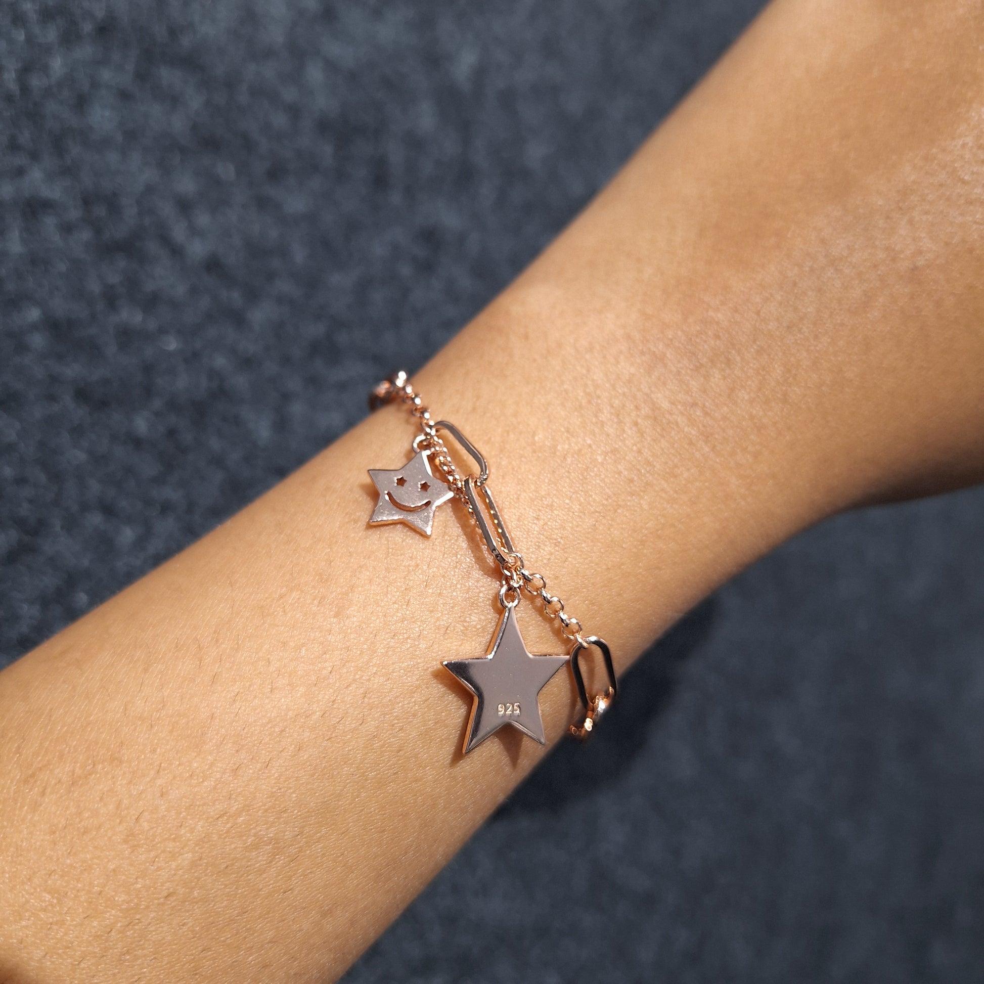 Rose gold bracelet with star charms on a wrist against a dark background