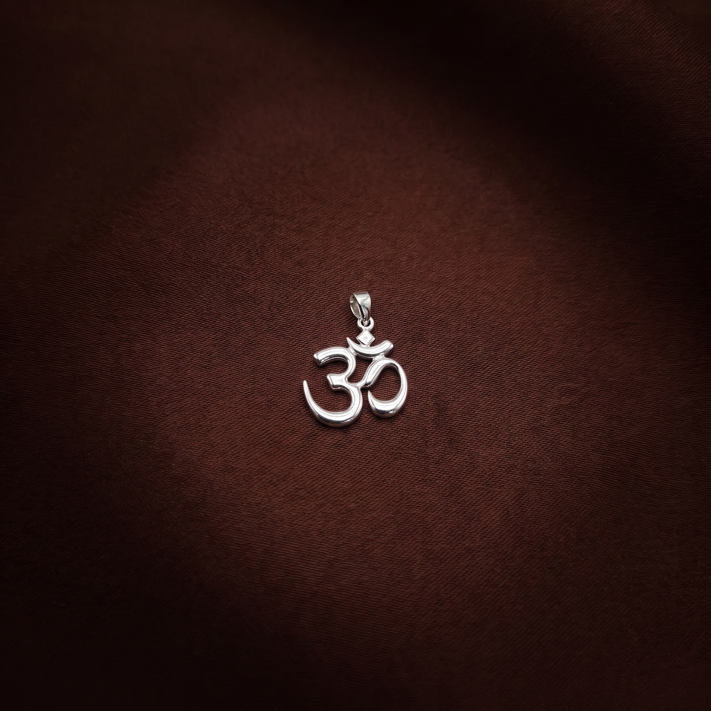 Silver Om symbol pendant on a brown fabric background