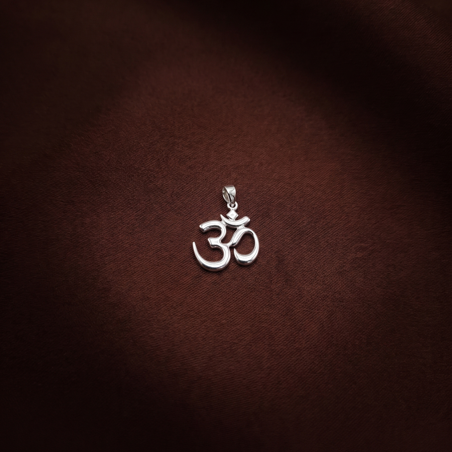 Silver Om symbol pendant on a brown fabric background