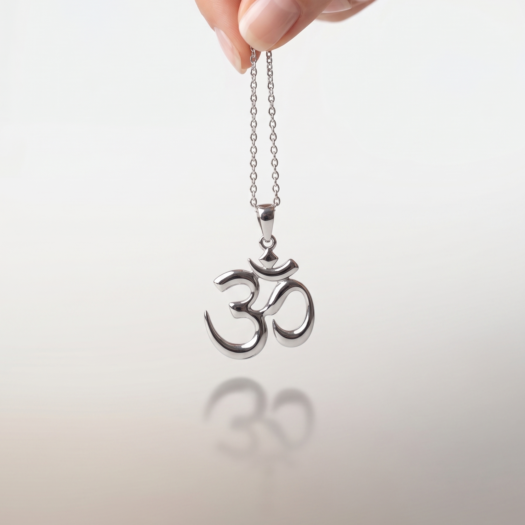 Silver Om pendant necklace held by a hand against a light background