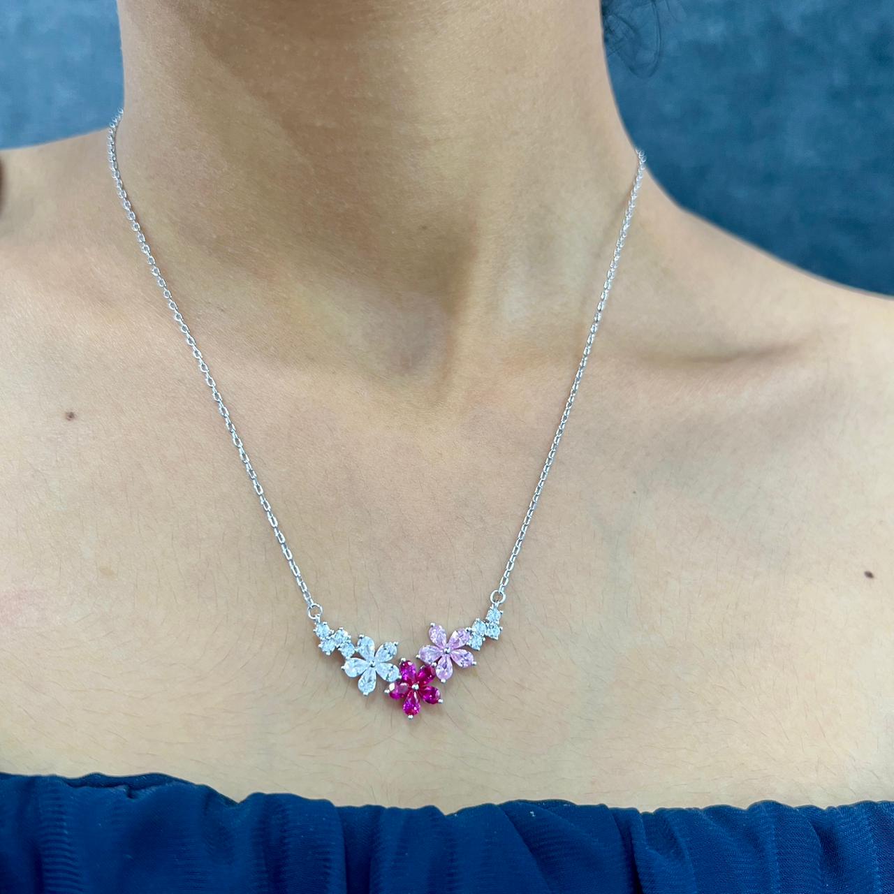 Necklace with floral design and gemstones worn by a person against a blue background