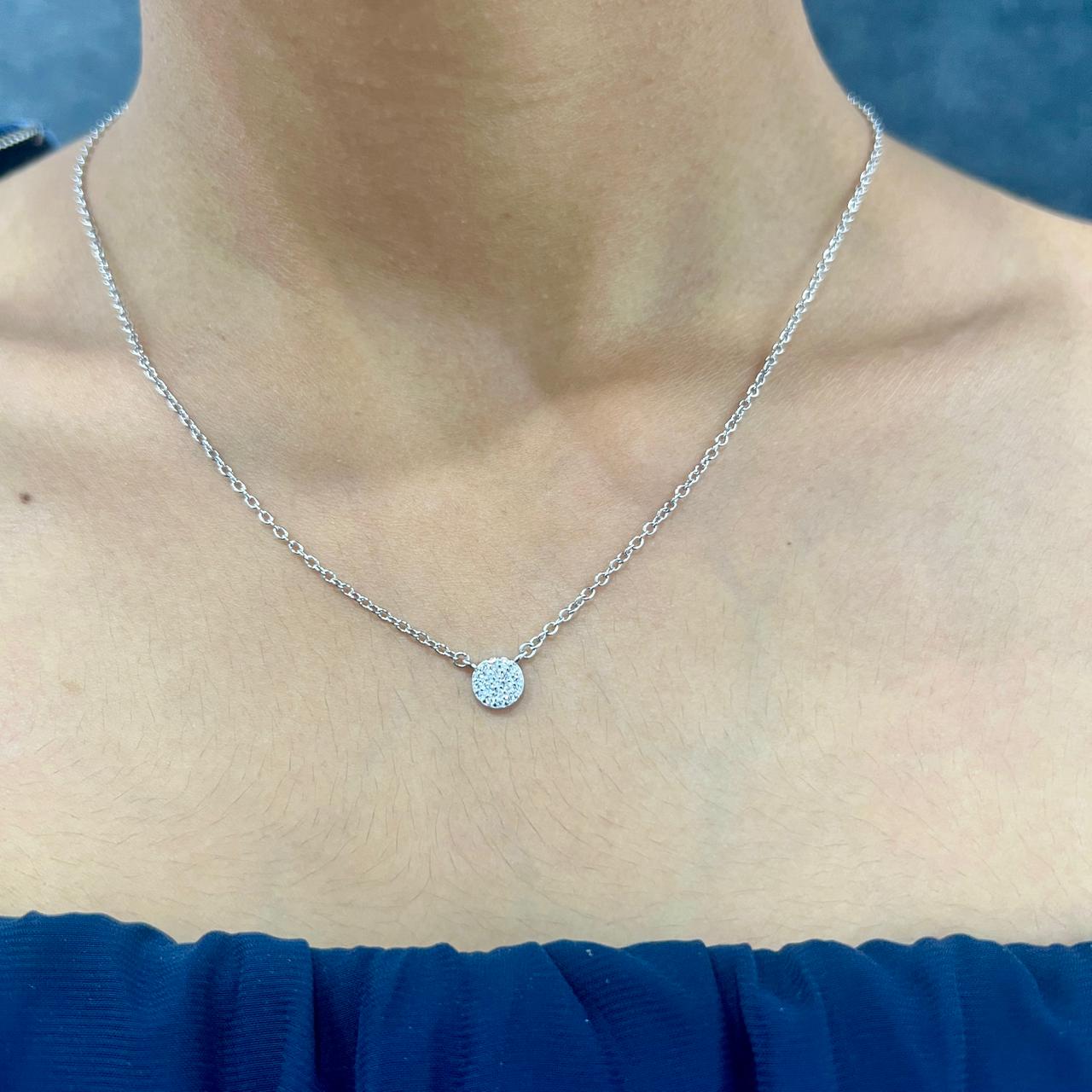Silver necklace with a round pendant on a person wearing a blue top.